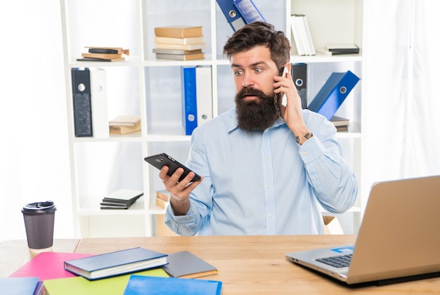 Hombre de negocios sorprendido hablando por teléfono celular usando un teléfono inteligente en la movilidad del escritorio de la oficina
