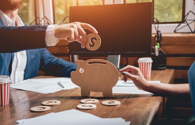 El hombre de negocios sostiene una moneda cerca de alcancía de madera.