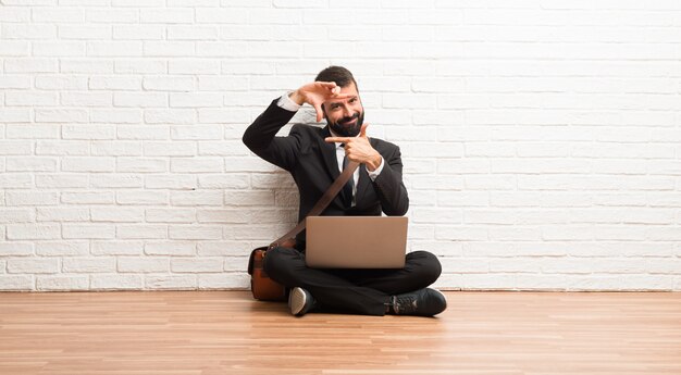 Hombre de negocios con su computadora portátil que se sienta en la cara de concentración del suelo. Símbolo de encuadre