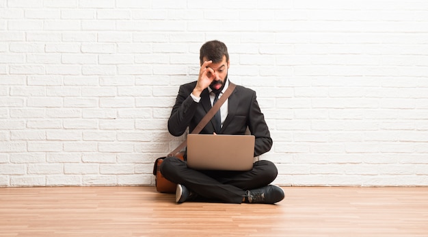 El hombre de negocios con su computadora portátil sentado en el suelo hace que la emoción de la cara sea divertida y loca