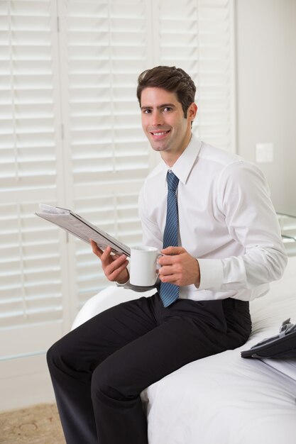 Hombre de negocios con taza de café y periódico en la habitación del hotel