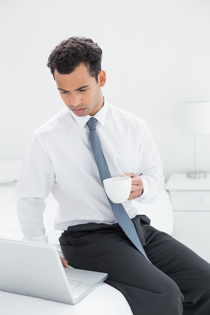 Hombre de negocios con taza de café usando la computadora portátil en la habitación de hotel