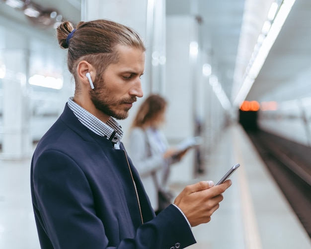 Hombre de negocios con un teléfono inteligente mientras espera un tren subterráneo