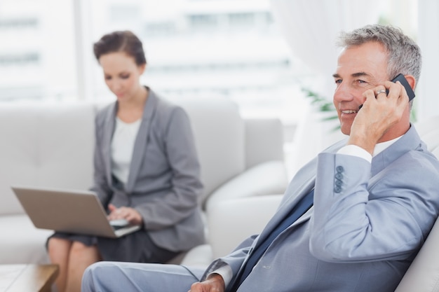 Hombre de negocios en el teléfono mientras su colega que trabaja en su computadora portátil