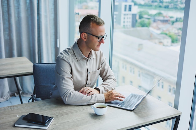 Un hombre de negocios trabaja en una computadora portátil Un gerente se sienta en una mesa en la oficina trabaja en una computadora portátil Empleado de lugar de trabajo independiente en trabajo remoto Lugar de trabajo remoto en café de coworking