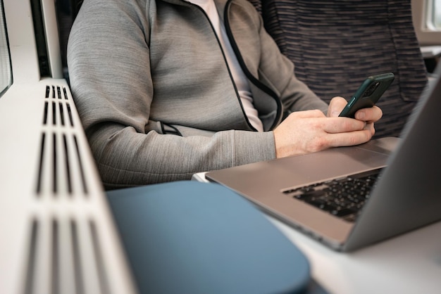 Un hombre de negocios trabaja sentado en un tren en la carretera usando un teléfono y una computadora portátil Viajar en Europa en tren Nómada digital de trabajo remoto