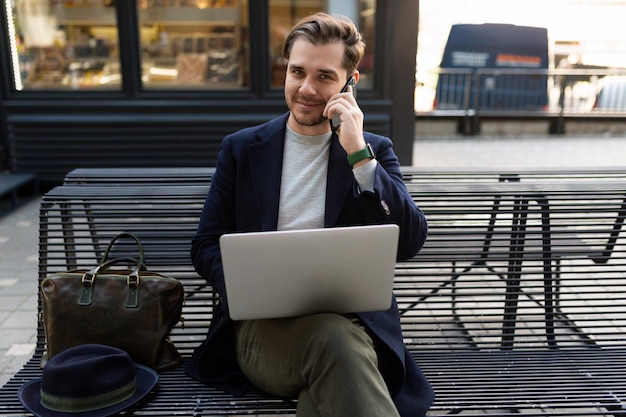 Hombre de negocios trabajando durante el almuerzo en una computadora portátil hablando por un teléfono móvil al lado de un café de la calle