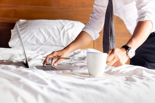 Hombre de negocios trabajando en cama con un portátil con una taza de café