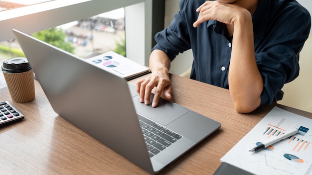 Hombre de negocios trabajando con datos gráficos en la computadora portátil y documentos en su escritorio en la oficina.