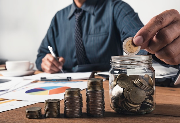 Hombre de negocios trabajando y escribiendo en el cuaderno con pila de monedas por concepto financiero y contable.