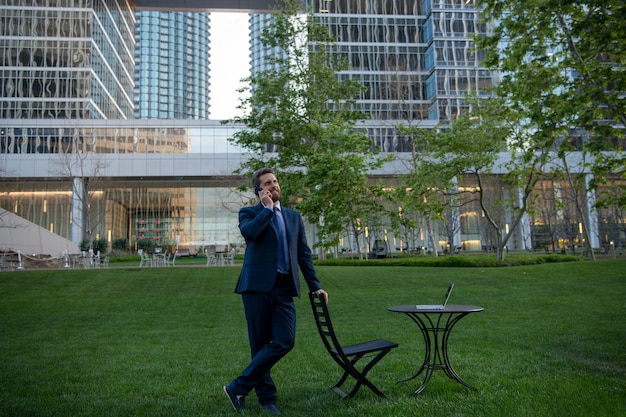 Hombre de negocios trabajando de forma remota en el parque moderno. Retrato de hombre de negocios sentado lugar de trabajo al aire libre en la terraza en el moderno centro de negocios.