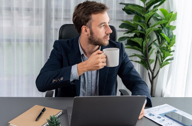 Hombre de negocios trabajando en su portátil y bebiendo café en su escritorio Entidad