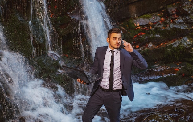 Hombre de negocios en traje con computadora portátil en el fondo de la cascada concepto de dispositivo impermeable empresario de teletrabajo