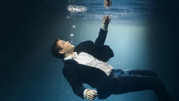 Un hombre de negocios con traje se está ahogando bajo el agua alcanzando la superficie del agua