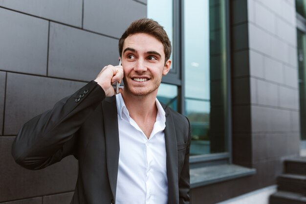 Hombre de negocios en traje hablando por teléfono y de pie cerca de la oficina