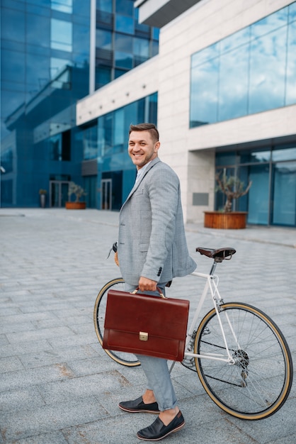 Un hombre de negocios en traje con maletín en bicicleta en el centro. Persona de negocios en transporte ecológico en las calles de la ciudad