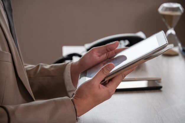 Hombre de negocios con traje marrón que trabaja con una tableta digital mientras está sentado en el escritorio de la oficina. Aplicación empresarial y concepto de tecnología digital.