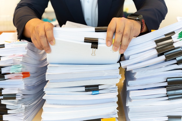 El hombre de negocios en traje mira a través de la pila de documentos en oficina.