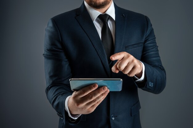 Un hombre de negocios en traje de negocios tiene un teléfono inteligente en sus manos.