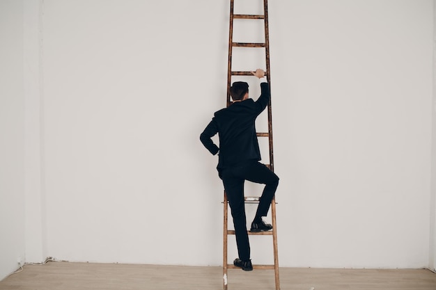 Foto hombre de negocios en traje negro levanta la escalera. carrera y crecimiento en el concepto empresarial. fondo blanco y espacio de copia.