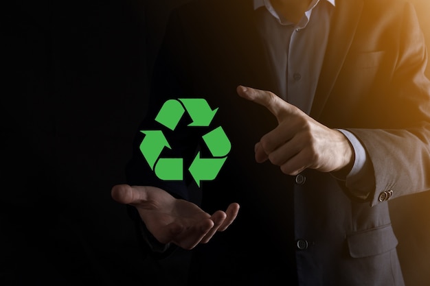 Hombre de negocios en traje sobre fondo oscuro tiene un icono de reciclaje, firme en sus manos. Concepto de ecología, medio ambiente y conservación. Luz azul roja neón