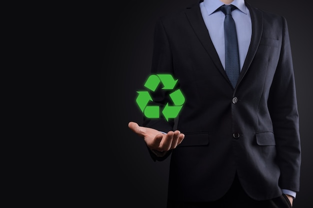 Hombre de negocios en traje sobre fondo oscuro tiene un icono de reciclaje, firme en sus manos. Concepto de ecología, medio ambiente y conservación. Luz azul roja neón