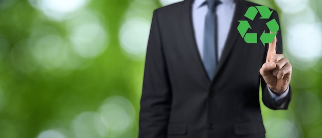 Hombre de negocios en traje sobre fondo verde natural tiene un icono de reciclaje, firme en sus manos.