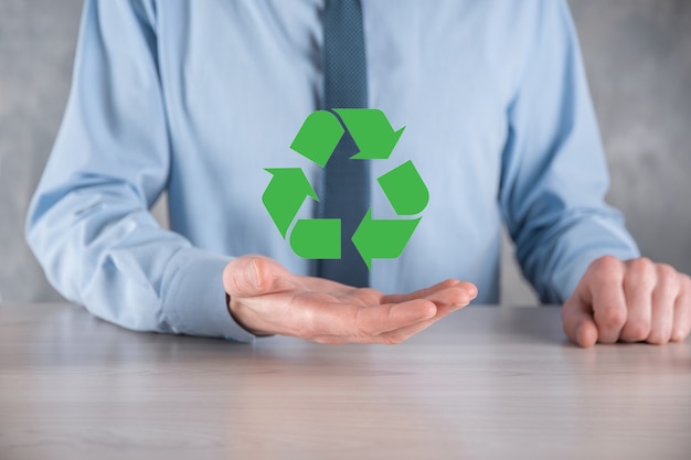 Hombre de negocios en traje sobre pared oscura tiene un icono de reciclaje, firme en sus manos. Concepto de ecología, medio ambiente y conservación. Luz azul roja neón.