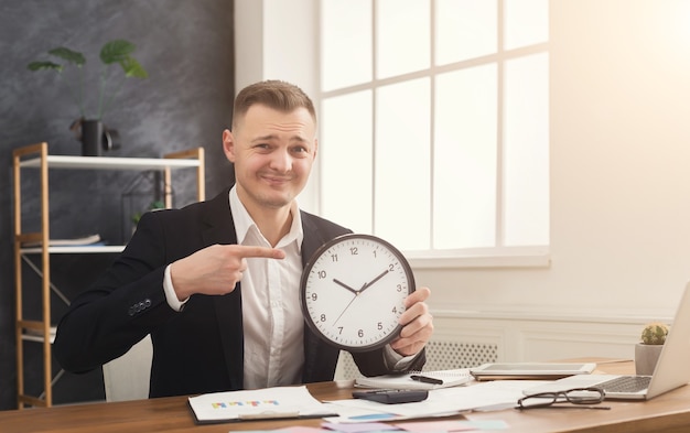 Foto hombre de negocios en traje sosteniendo el reloj y apuntando en él. retrato de hombre con relojes en la oficina. gestión del tiempo y falta de concepto de tiempo, espacio de copia