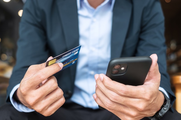 Hombre de negocios en traje con tarjeta de crédito y uso de teléfono inteligente con pantalla táctil para compras en línea mientras realiza pedidos en la cafetería u oficina .Negocio, tecnología, comercio electrónico y concepto de pago en línea