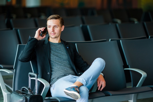 Hombre de negocios urbanos hablando por teléfono inteligente viajando dentro en el aeropuerto. hombre joven con teléfono móvil en el aeropuerto esperando el embarque.