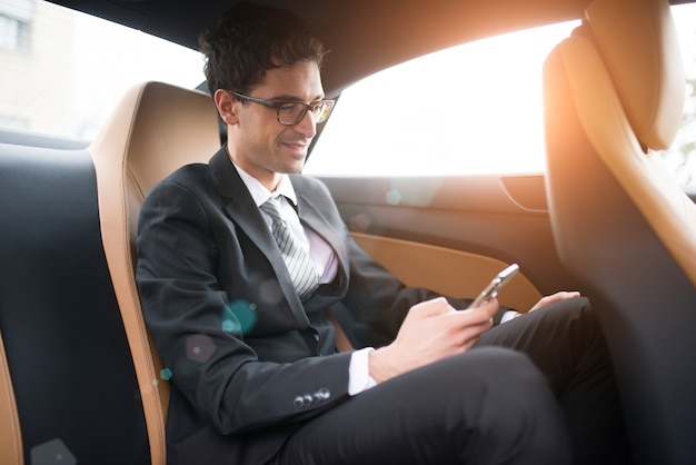 Hombre de negocios usando su teléfono móvil en el asiento trasero de un automóvil