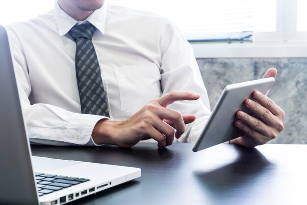 Hombre de negocios usando la tableta y la computadora portátil en el escritorio.