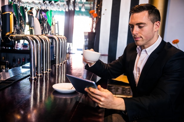 Hombre de negocios usando tableta tomando un café en el mostrador en un bar