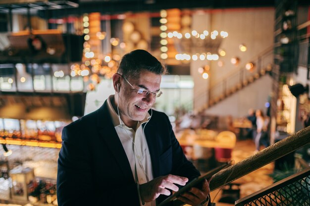 Hombre de negocios usando tableta para video llamada mientras está de pie en la cafetería.