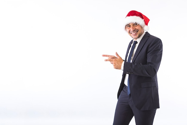 Hombre de negocios vestido con traje, corbata y sombrero de Navidad de Santa Claus, sonriendo, apuntando con las manos, sobre fondo blanco. Concepto de celebración de Navidad.