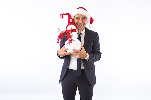 Hombre de negocios vestido con traje, corbata y sombrero de Navidad de Santa Claus, sonriendo con un muñeco de nieve, sobre fondo blanco. Concepto de celebración de Navidad.