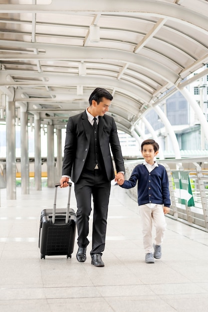 Un hombre de negocios vestido con un traje con una maleta tomó la mano de su adorable hijo. y caminar juntos a lo largo del corredor del tren aéreo le sonrió felizmente a su hijo - concepto de padre e hijo de familia feliz