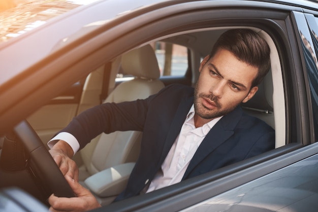 Hombre de negocios en la vista trasera del coche del joven guapo mirando a la derecha mientras conduce