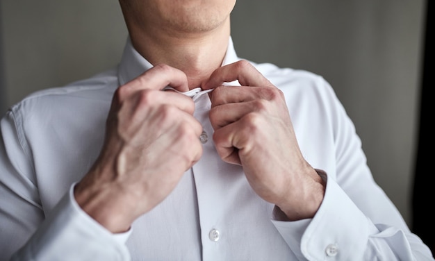 El hombre de negocios se viste de camisa blanca, primer plano de las manos masculinas, el novio preparándose en la mañana antes de la ceremonia de la boda