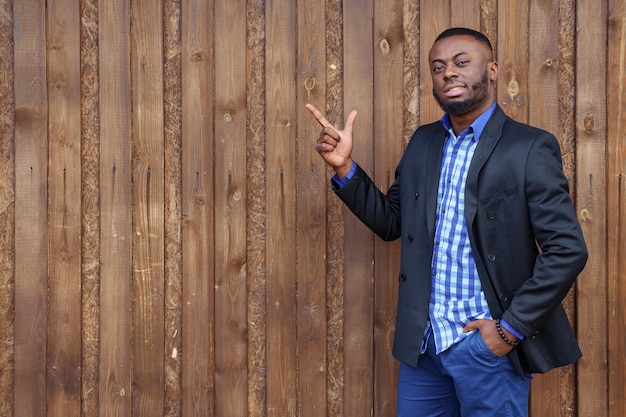 Hombre negro africano con barba apuntando hacia el lado con el dedo sobre fondo de madera, copyspace. Él sonriendo y mirando a la cámara.