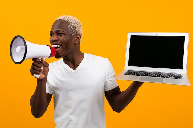 Hombre negro africano con cabello blanco habla en un megáfono sosteniendo un laptopp para publicidad en un estudio amarillo