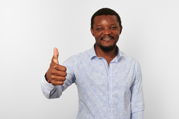 Hombre negro afroamericano feliz con los pulgares hacia arriba como gesto en un fondo blanco casual de camisa brillante