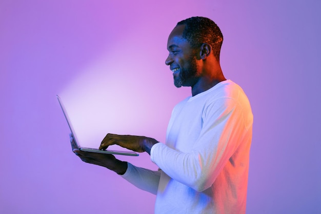 Hombre negro alegre que usa una computadora portátil moderna con una pantalla brillante