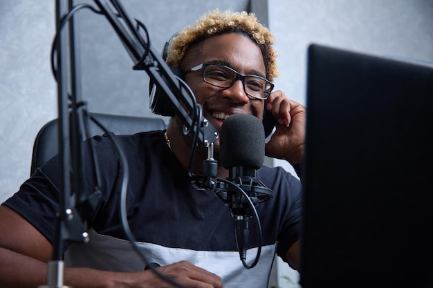 Un hombre negro alegre y sonriente con auriculares y un micrófono profesional graba un podcast de audio para la transmisión en vivo de radio en Internet, el presentador presenta las noticias en vivo