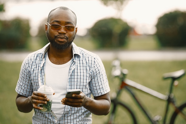 Hombre negro americano de pie sobre un césped y usando un teléfono. Hombre vestido con camiseta blanca y camisa a cuadros azul