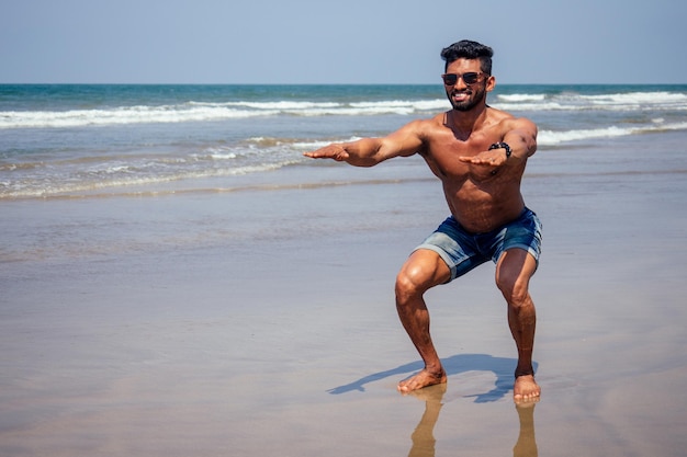 Hombre negro atlético, musculoso y saludable en topless, instructor de calentamiento en la playa.Modelo de moda masculino indio con pantalones cortos de mezclilla, jeans y cuerpo perfecto.Alimentos saludables y vacaciones activas en la playa.