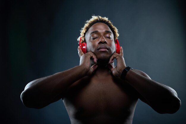 El hombre negro con auriculares inalámbricos rojos escucha música y disfruta de la música en un fondo negro