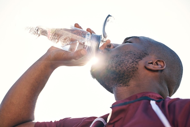 Hombre negro bebiendo agua y salud con atleta de fitness y deportes con hidratación y sol Bebida de hombre africano en botella y bienestar con destello de lente de ejercicio y ángulo bajo