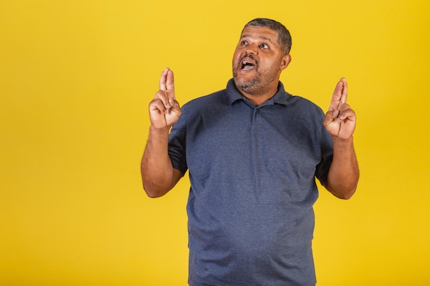 Hombre negro brasileño adulto sonriendo dedos cruzados deseando señal de suerte